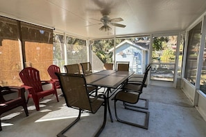 Une terrasse couverte avec une table et des chaises, de grandes fenêtres et un ventilateur de plafond.