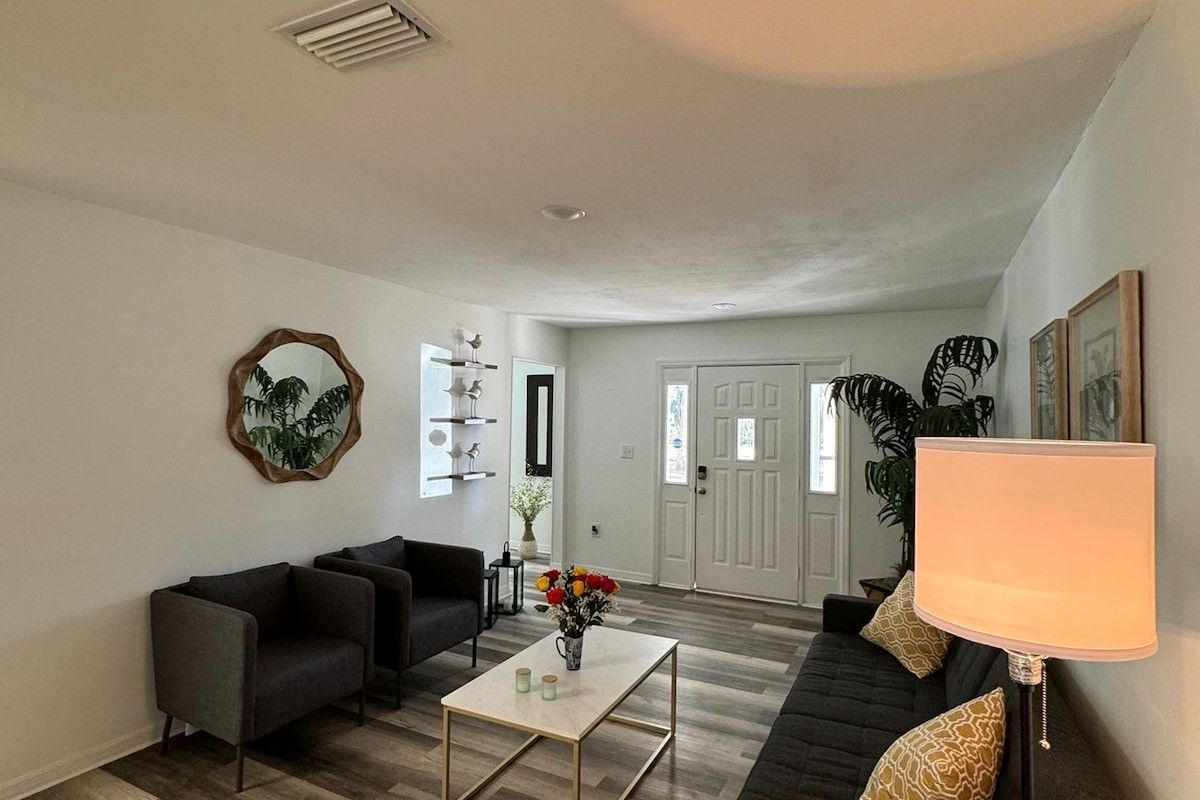 Un salon avec un canapé, une table basse et une lampe. On aperçoit une porte et une plante au fond.