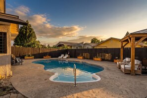 Un patio trasero con piscina, sillas de descanso y una terraza de madera.