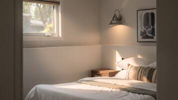 A bedroom with a bed, bedside table, lamp, and a window.