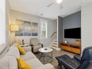 Ein modernes Wohnzimmer mit einer Couch, Sesseln, einem Couchtisch und einem Flachbildfernseher.