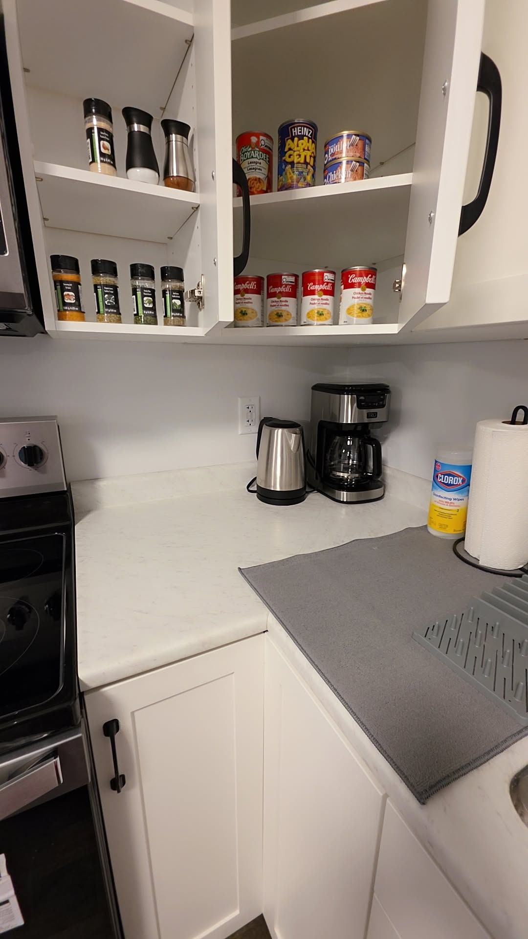 A kitchen with a stove, coffee maker, and various food items on shelves.