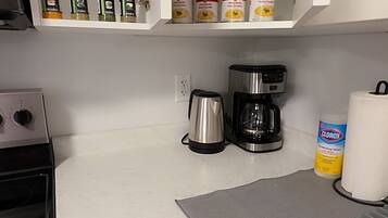 A kitchen with a stove, coffee maker, and various food items on shelves.