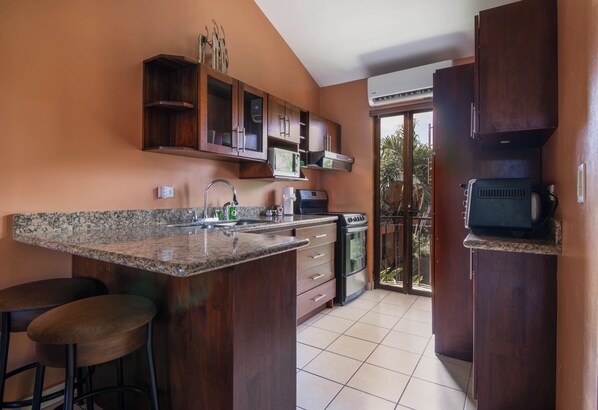 A kitchen with a granite countertop, stainless steel appliances, and wooden cabinets. - Pool Below, Laundry In, Sleeps 6: Casa Jade (Playas del Coco)