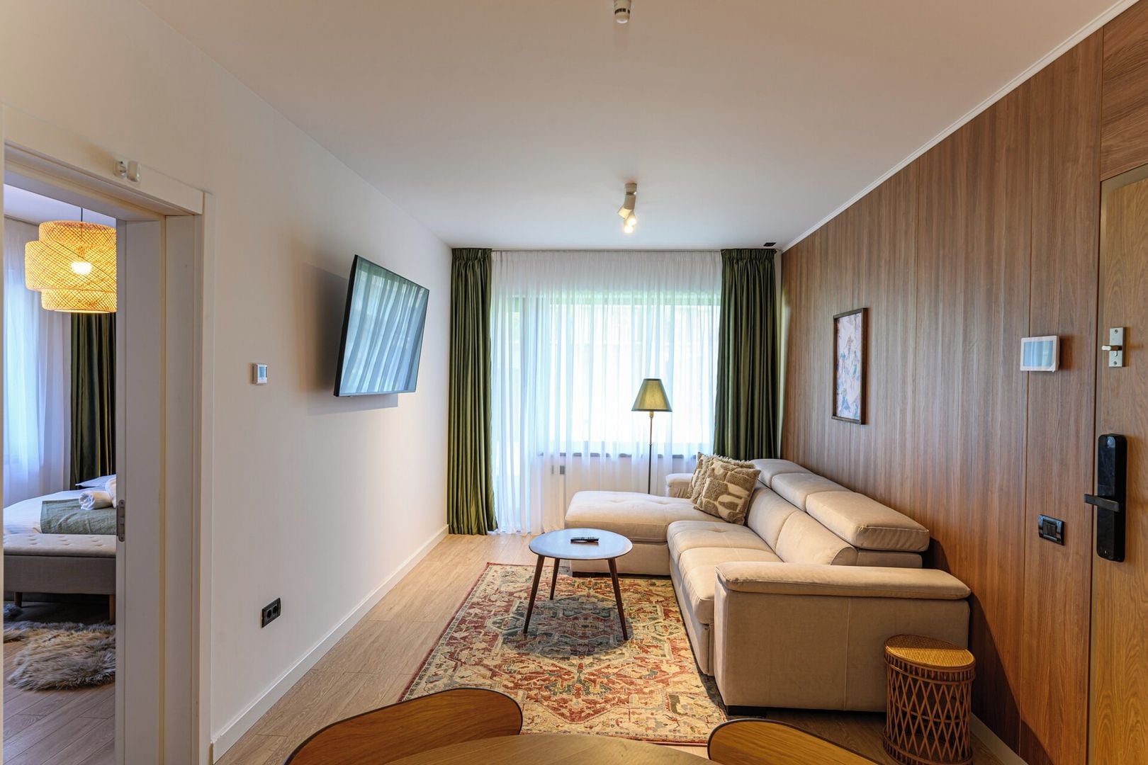 Una habitación de hotel moderna con sofá, una mesita, televisor y un muro decorativo de madera.