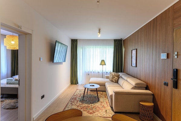 Una habitación de hotel moderna con sofá, una mesita, televisor y un muro decorativo de madera.
