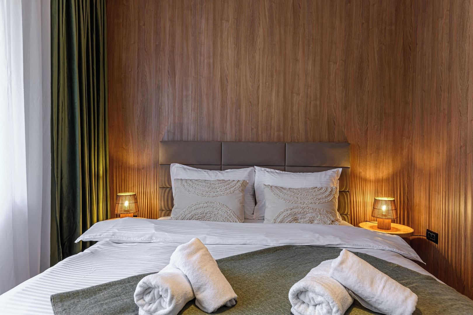 Soft sage and warm wood tones create a soothing bedroom palette — layered pillows, upholstered headboard and bedside lighting for a premium mountain stay. Slopeview Chalet.
