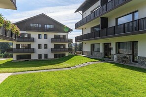 Un edificio residencial moderno de dos pisos con balcones, un césped cuidado y fachada de piedra.