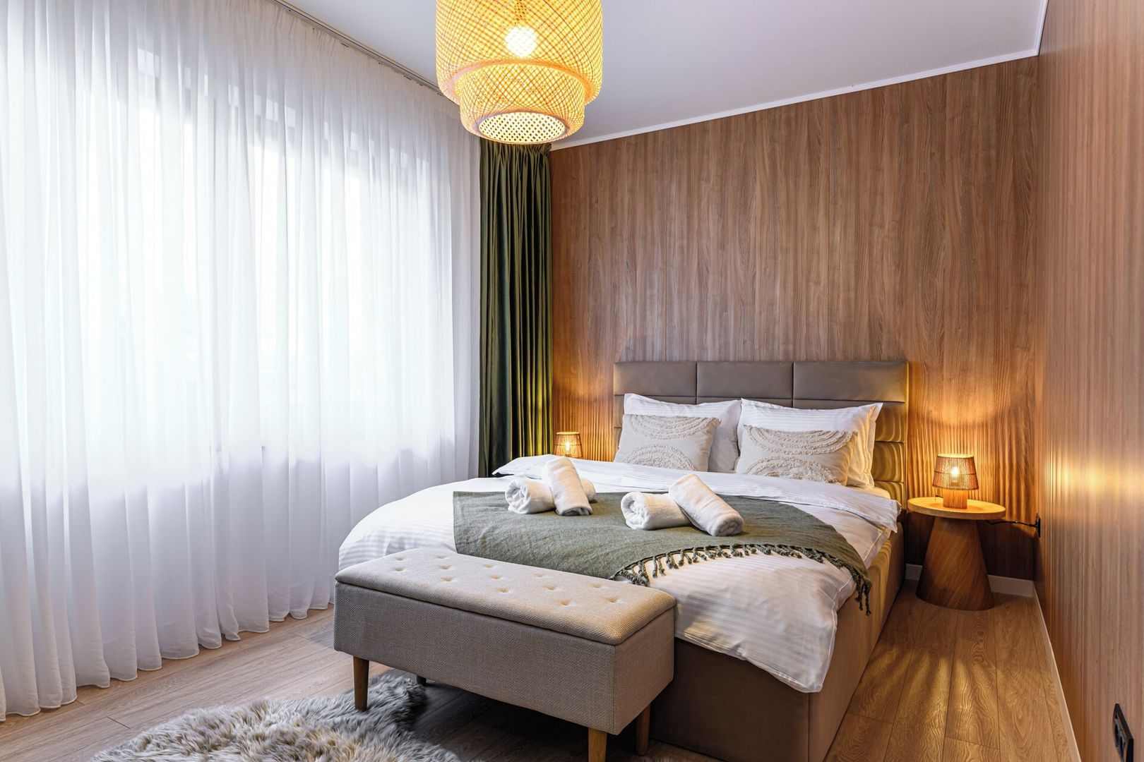 Una camera da letto moderna con un letto grande, un comodino, una lampada a sospensione e vista all'esterno attraverso tende leggere.