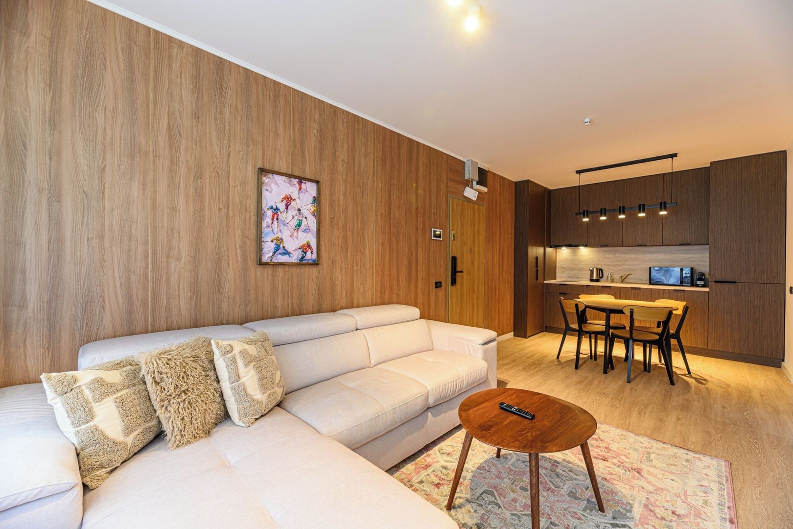 A modern living room with a white sofa, a coffee table, and a kitchen area with wooden cabinets and a dining table.