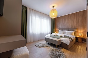 Un dormitorio moderno con cama, mesitas de noche, un sofá y un ventanal con cortinas.