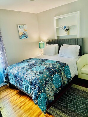 Een slaapkamer met een bed, een nachtkastje, een lamp, een schilderij aan de muur en een raam met uitzicht.