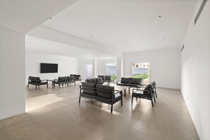 A spacious, modern interior with a minimalist design, featuring a large seating area with sofas and chairs, a flat-screen TV mounted on the wall, and large windows providing natural light. - Los Cabos Chic Stay Walk to Beach & Nightlife (Cabo San Lucas)