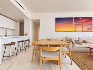 Een modern interieur met een houten eettafel, barkrukken, een bank en een groot schilderij van een zonsondergang.
