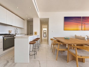 A modern kitchen with a central island, bar stools, and a dining area with wooden chairs. - Los Cabos Chic Stay Walk to Beach & Nightlife (Cabo San Lucas)
