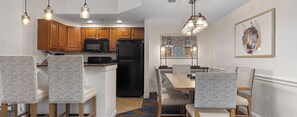 A kitchen with wooden cabinets, a microwave, and a black refrigerator. There is a dining area with a table and chairs. - Disney in Luxury! Spring Break 3/13-3/16. Rare RESORT find. For 4. Full Kitchen (Lake Buena Vista)