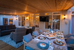 Ein Essbereich im Freien mit einer Holzterrasse, Korbmöbeln und einem für eine Mahlzeit gedecktem Tisch.
