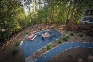 Ein bewaldetes Aussenareal mit Feuerstelle, Sitzgelegenheiten und einer Holzterrasse.