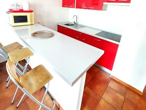 A kitchen with a white countertop, red cabinets, and a stainless steel sink. There are three stools and a microwave on the counter. - MAREVERDE WIFI FREE & POOL VIEW (Costa Adeje)