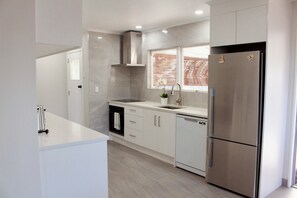 A modern kitchen with stainless steel appliances, white cabinetry, and a window with blinds. - Sunny modern 3BR home in Napier - Near supermarket, dining and parks (Napier)