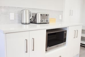 A kitchen with white cabinets, a stainless steel kettle, a toaster, and a microwave. - Sunny modern 3BR home in Napier - Near supermarket, dining and parks (Napier)