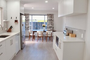 A modern kitchen with white cabinetry, a dining area with a table and chairs, and a view through the window. - Sunny modern 3BR home in Napier - Near supermarket, dining and parks (Napier)