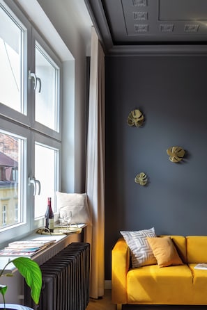 A room with a yellow sofa, a radiator, a window with curtains, and a wall with decorative leaf patterns. - Eclectic 2-bed apartment by Fragola (Kraków)