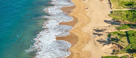An aerial view of a beach with clear blue water, sandy shore, and a few people.