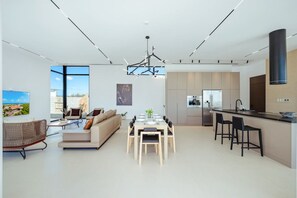 A modern kitchen with a central island, a dining area with a table and chairs, and a living area with a sofa and a TV. - NEW 4BR Luxury Villa | Pool | Tierra del Sol - Catalina 34 by Bocobay (Noord)