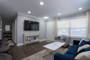 Una sala de estar con una mesa de centro blanca, un sofá gris y un televisor montado en la pared.