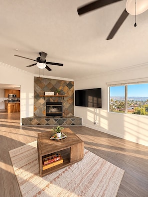 A modern living room with a fireplace, a television, and a view of a cityscape. - Panoramic Views, Outdoor Kitchen & Spacious 3BR Home (Spring Valley)