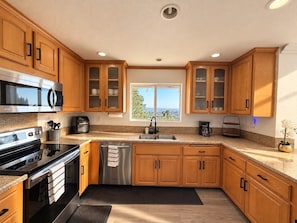 A kitchen with wooden cabinets, stainless steel appliances, a window with a view, and a black rug. - Panoramic Views, Outdoor Kitchen & Spacious 3BR Home (Spring Valley)