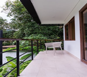 A balcony with a white chair, a metal railing, and a view of lush greenery.