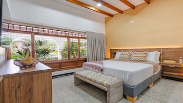 A bedroom with a bed, bedside table, bench, and a view of a garden through large windows.