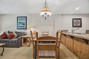 A compact living space with a kitchenette, a dining table with chairs, a sofa, and a hanging light fixture. - Private Patio on Ski-Back Run · Ground-Floor 1BR · Gondola Walkway & Heated Pool (Breckenridge)