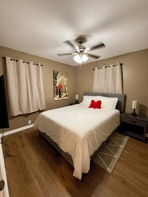 A bedroom with a bed, a ceiling fan, a nightstand, a lamp, and a painting on the wall. - Peaceful 3-BR House in Vibrant Memphis (Memphis)
