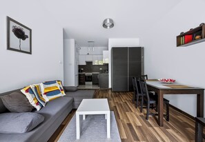 A modern living room with a grey sofa, a white coffee table, and a dining area with a wooden table and chairs. - Zielony Żoliborz Urban Apartment (Warszawa)