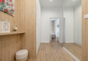 Ein Flur mit Holzboden, einer weißen Bank und einer Tür zu einem Schlafzimmer mit Bett und Vorhängen.