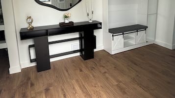 A room with a wooden floor, a black console table with a mirror, a white coat rack, and a bench.