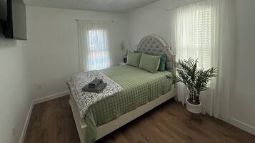 A bedroom with a bed, a ceiling light fixture, a potted plant, and a window with curtains.