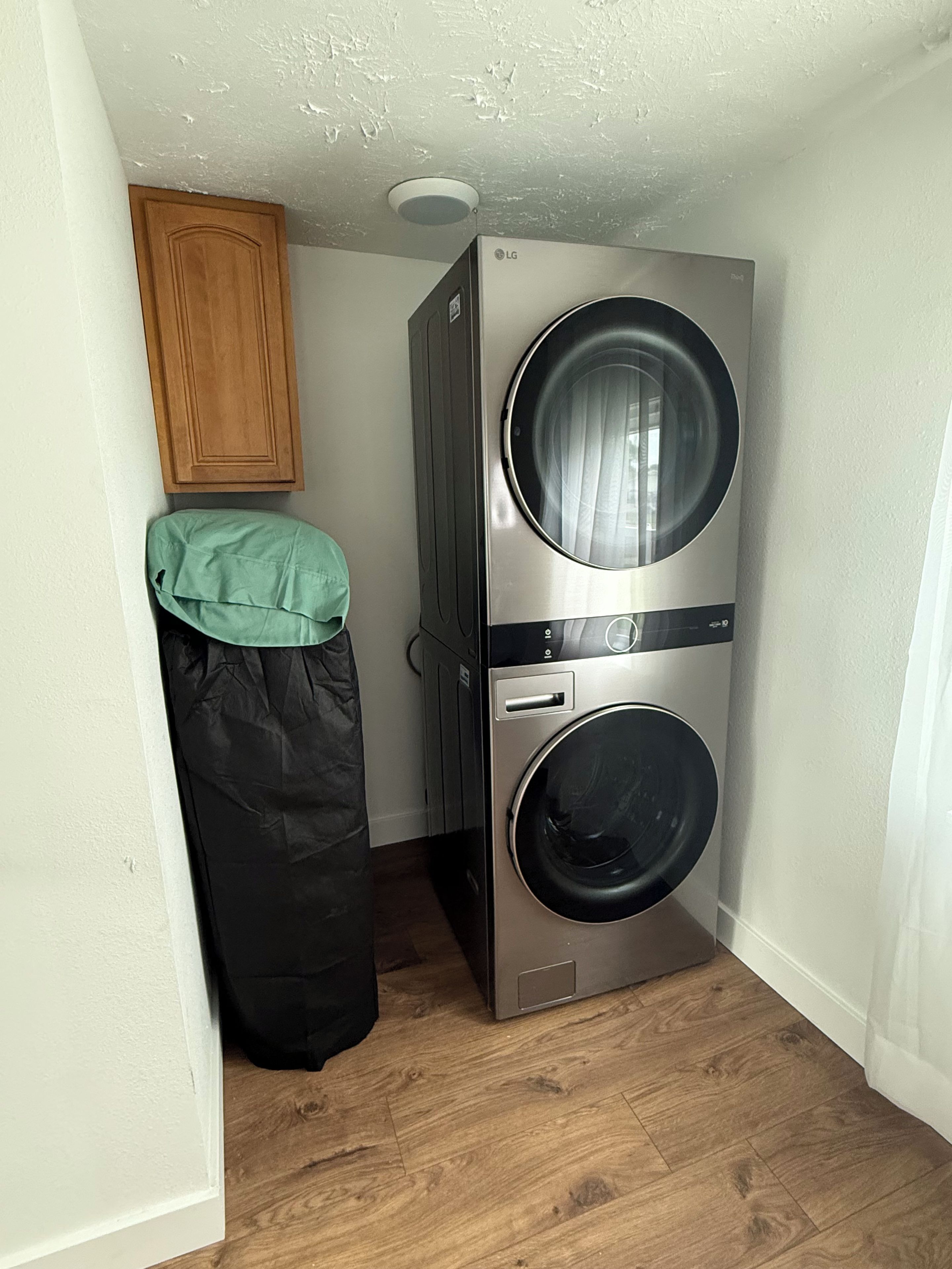 A compact laundry room with a stacked washer and dryer, wooden cabinets, and a green towel on a hook.