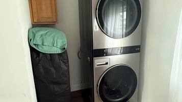 A compact laundry room with a stacked washer and dryer, wooden cabinets, and a green towel on a hook.