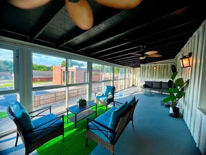 Een overdekt terras met rieten meubilair en kunstgras.