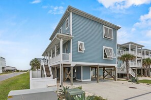 Ein zweistöckiges Strandhaus mit überdachter Veranda und einer kleinen Treppe, die zum oberen Stock führt.