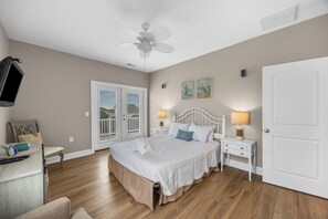 Ein Schlafzimmer mit Bett, Nachttischlampen, Deckenventilator, Fernseher und einer Tür.