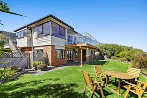 A two-story house with a balcony, a patio with a table and chairs, and a well-maintained lawn. - Beachfront Home at Tata Beach (Tata Beach)