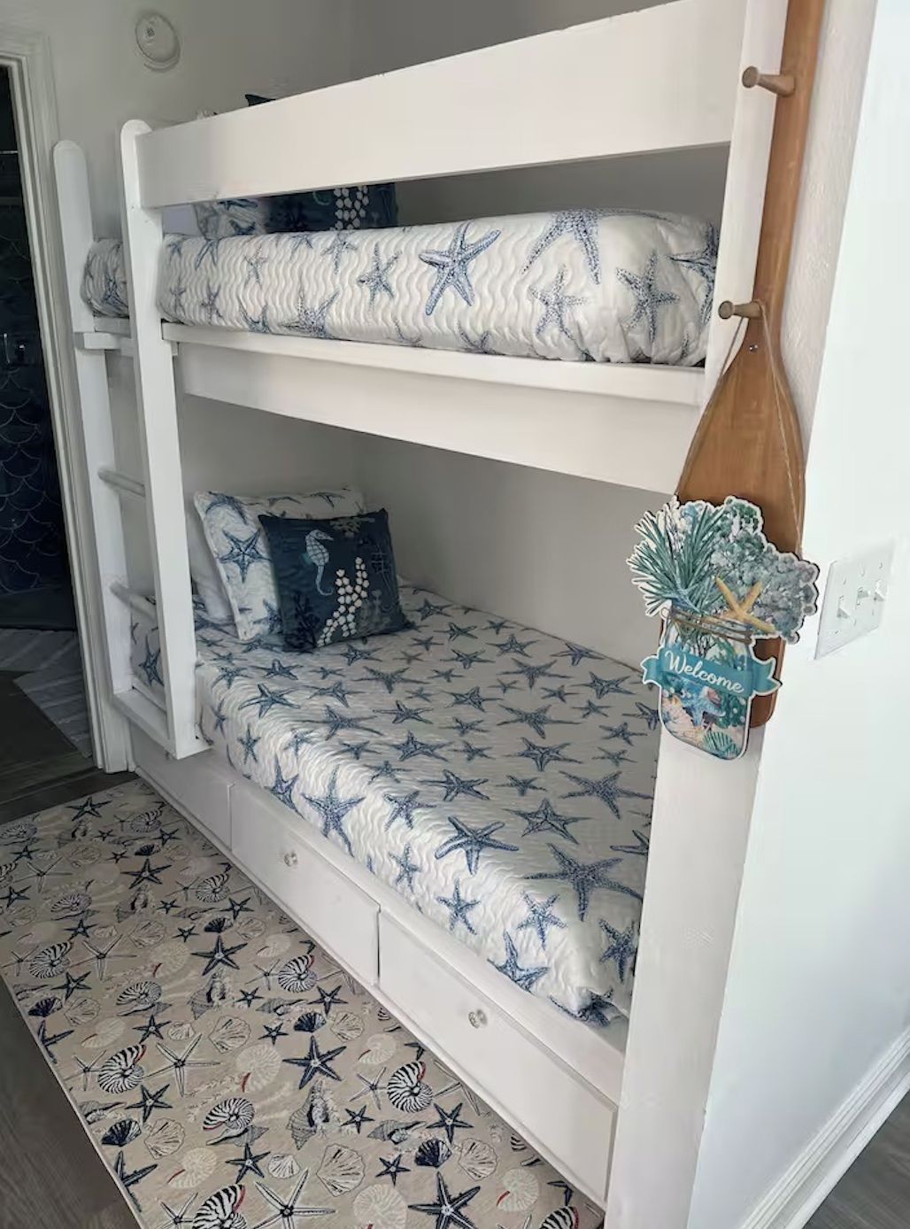 A bunk bed with a starfish pattern, a welcome sign, and a decorative pinecone.