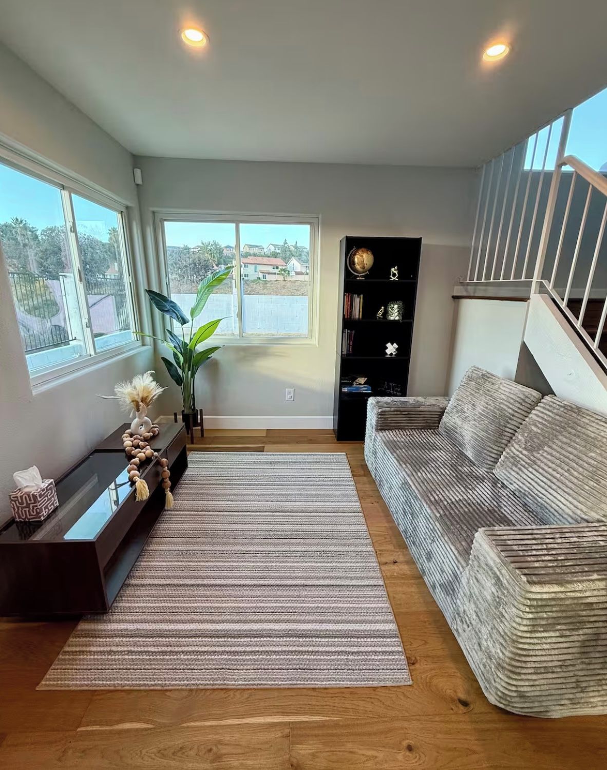 A living room with a sofa, a coffee table, a bookshelf, a plant, and a staircase.