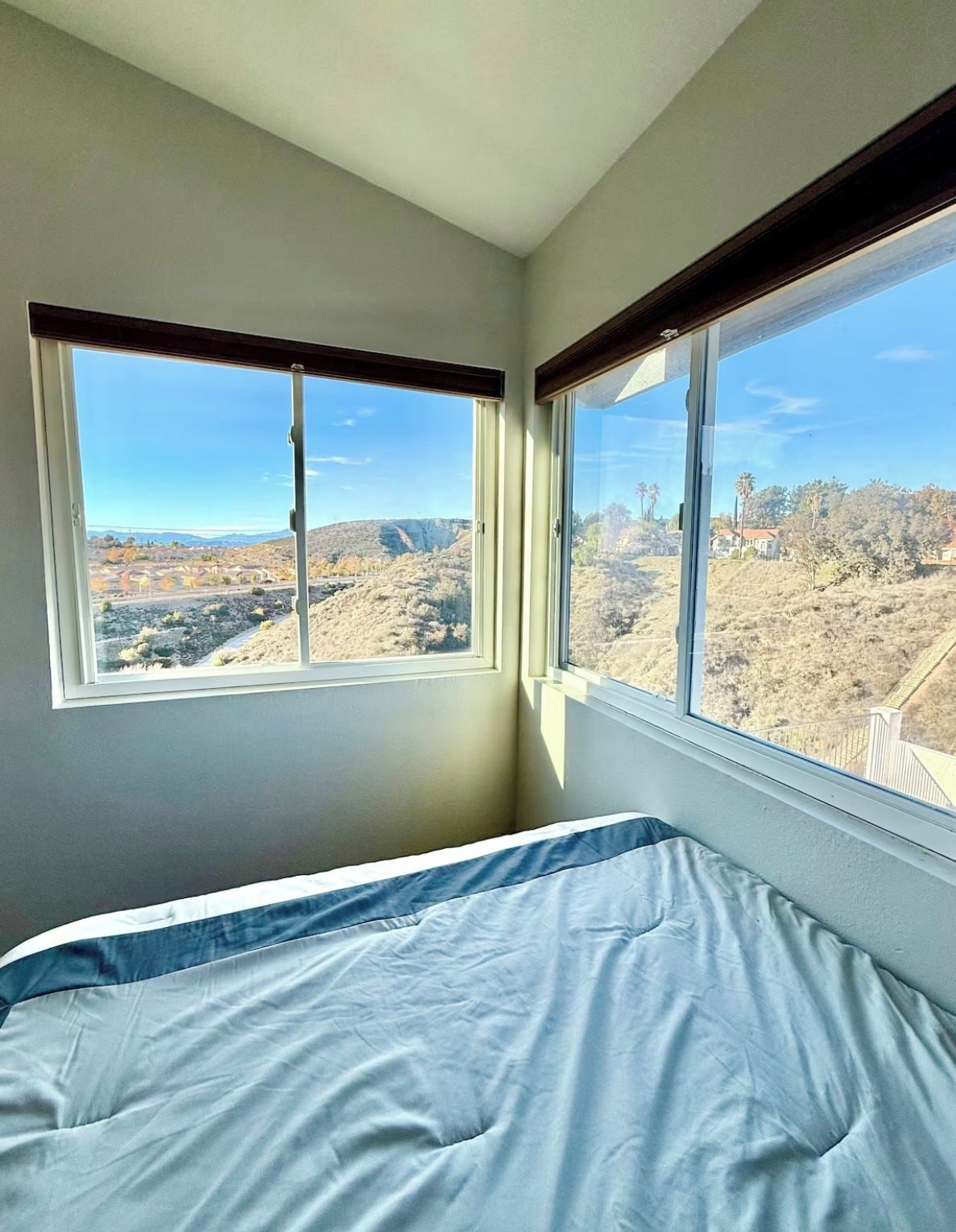 A bedroom with a bed, two windows, and a view of a hilly landscape.