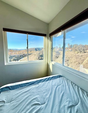 Une chambre à coucher avec un lit, deux fenêtres et une vue sur un paysage vallonné.